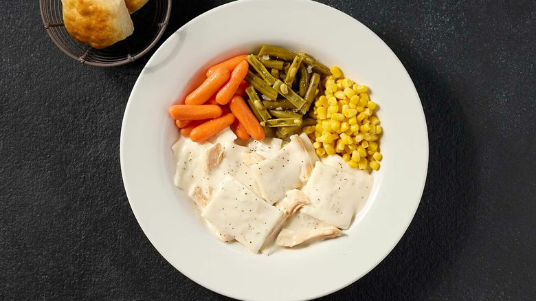 A plate of chicken and dumplings with carrots, green beans, and corn on a black table