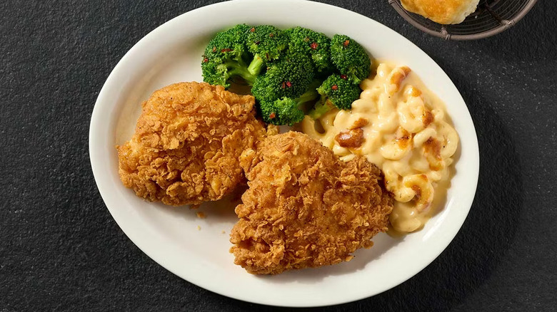 Crispy fried chicken on a white plate with mac and cheese and broccoli on a black table