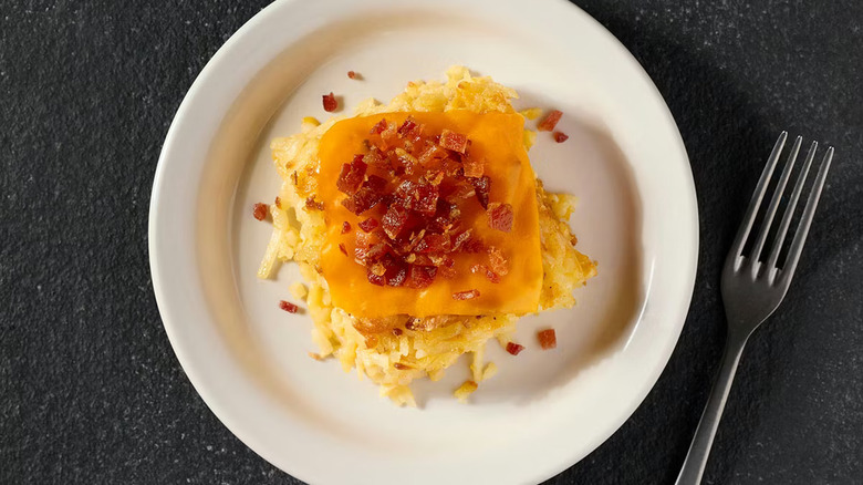A loaded hashbrown casserole from Cracker Barrel on a white plate placed on a black table with a fork