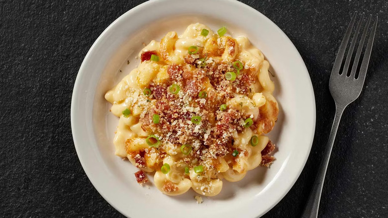 A white plate full of bacon mac and cheese on a black table with a fork on the side