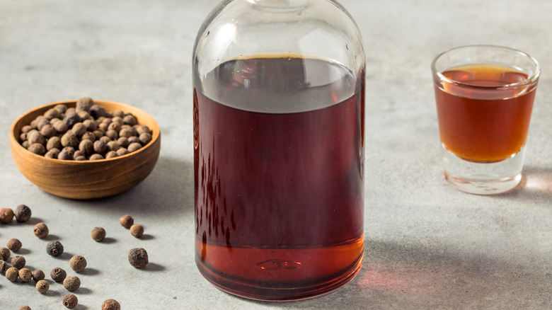 A bottle and glass of allspice liqueur, next to a bowl of allspice berries