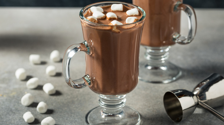 Glass mugs of hot cocoa with marshmallows, next to a bar jigger