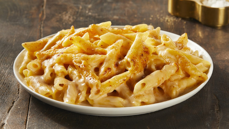 A plate of macaroni and cheese made with penne pasta on a wooden table