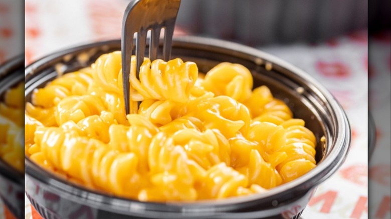 A fork reaching down into a black bowl of mac and cheese made with rotini pasta