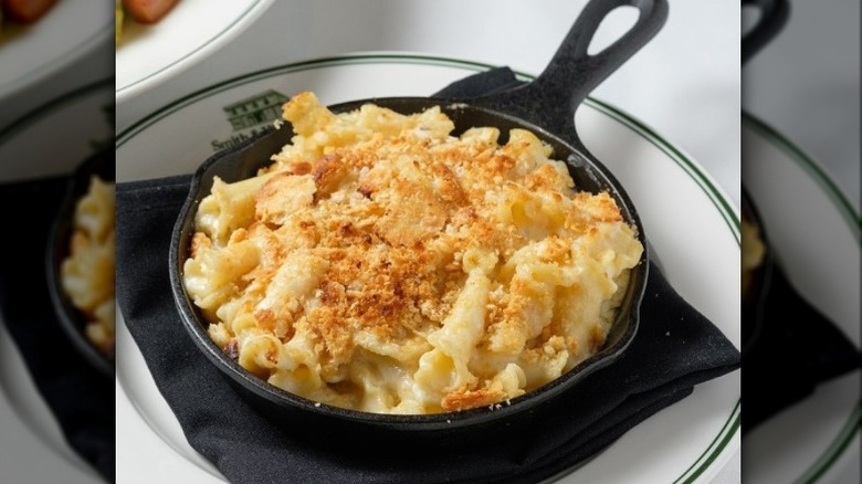 A small cast iron skillet with a breadcrumb-topped mac and cheese served over a black napkin on a white plate with Smith & Wollensky branding