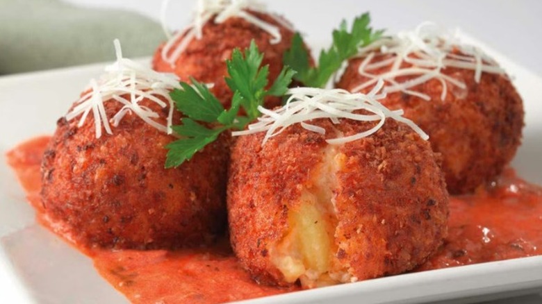 A white plate with a bed of marinara sauce with four friend mac and cheese balls, topped with shredded cheese and parsley