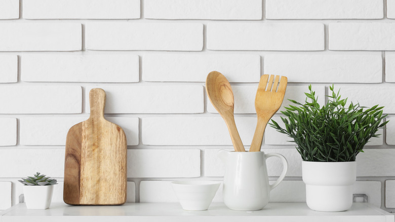 A kitchen shelf, with fake plants and wooden utentils