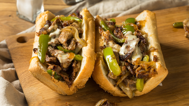 A philly cheesesteak filled with thinly sliced stead, onions, peppers, and melted cheese on a wood cutting board