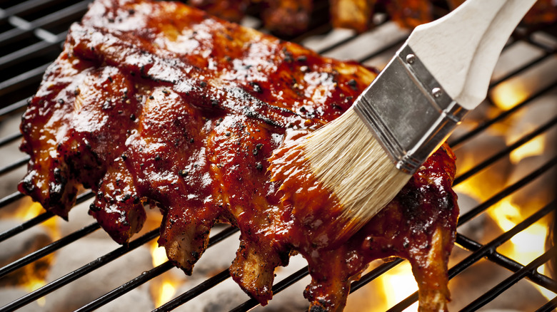 A person brushes barbecue sauce onto a rack of ribs