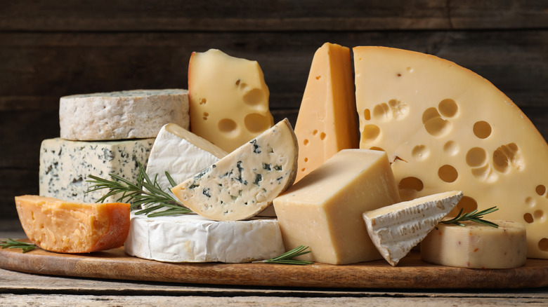 A group of different cheeses piled together on a wooden board against a wooden background