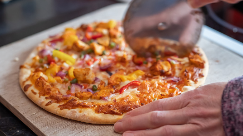 Pizza with chicken and bell peppers being slice on a cutting board