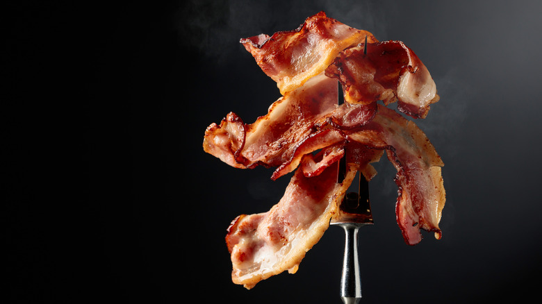 Pieces of bacon skewered on a two-pronged fork in front of a black background