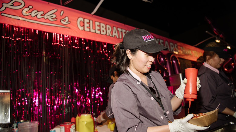 A worker at Pink's Hot Dogs making a hot dog