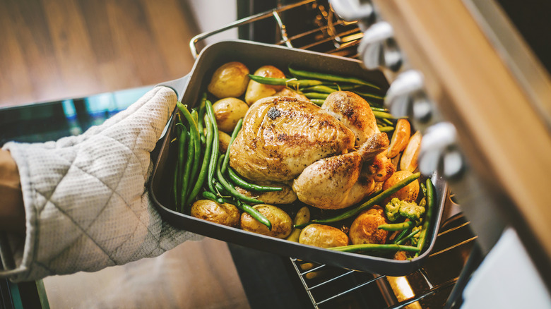 Person taking chicken roast on vegetables out of oven