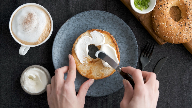 Hands spreading cream cheese on bagel