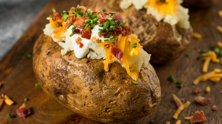 Two loaded baked potatoes with cheese, bacon, and chives