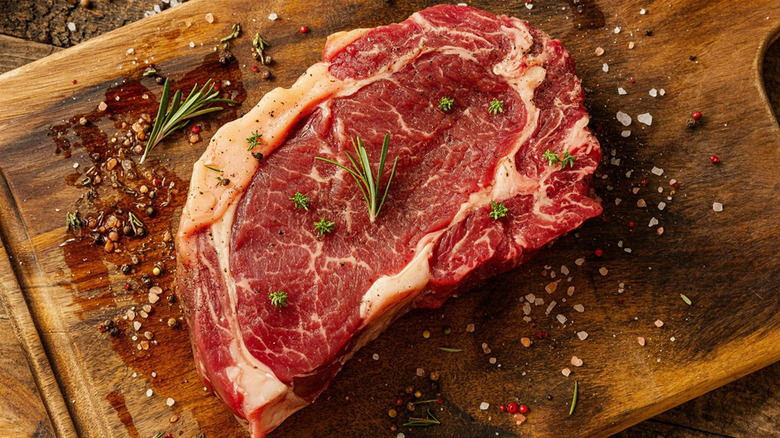 A raw ribeye on a cutting board with sprigs of rosemary and spices