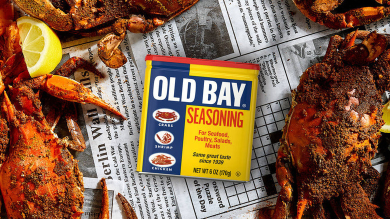 A tin of Old Bay on a piece of newspaper surrounded by seasoned crabs