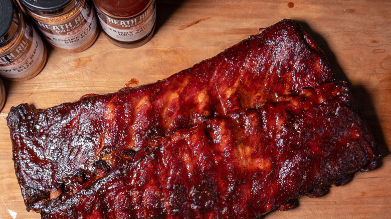 A beautifully glazed rack of ribs next to bottles of Heath Riles rubs