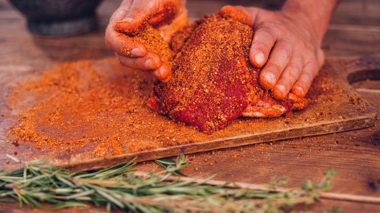 Hands seasoning a piece of meat with generous amounts of rub