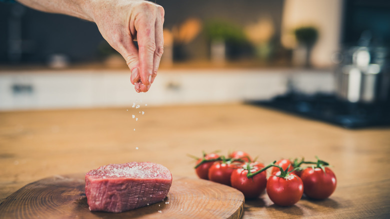 A hand sprinkling salt over a steak from six inches in the air