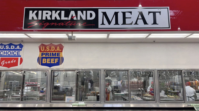 A shot of the Costco meat section with a red banner reading "Kirkland Signature Meat" and a window with butchers below