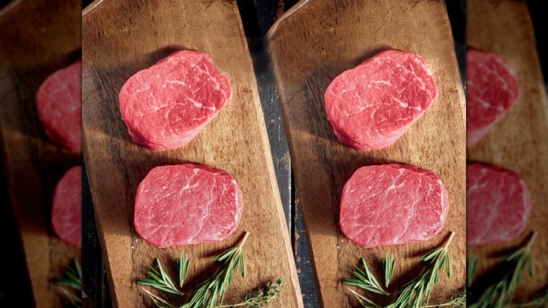 Four raw filet mignon steaks on two wooden cutting boards