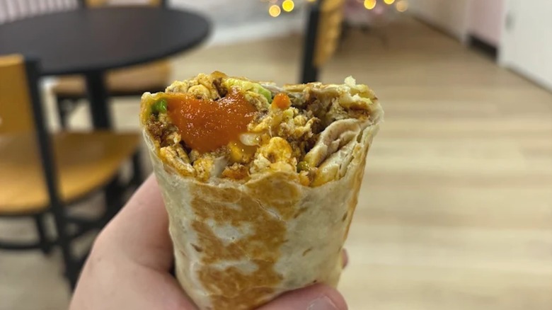 Person's hand holding breakfast burrito with bite taken from it