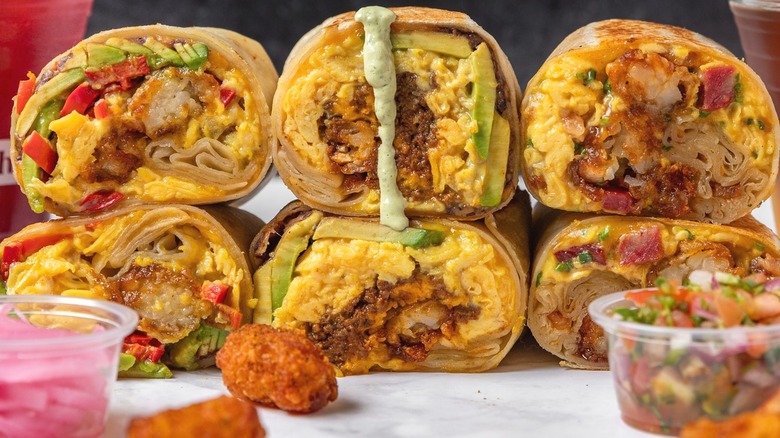 Several halved breakfast burritos with cups of toppings