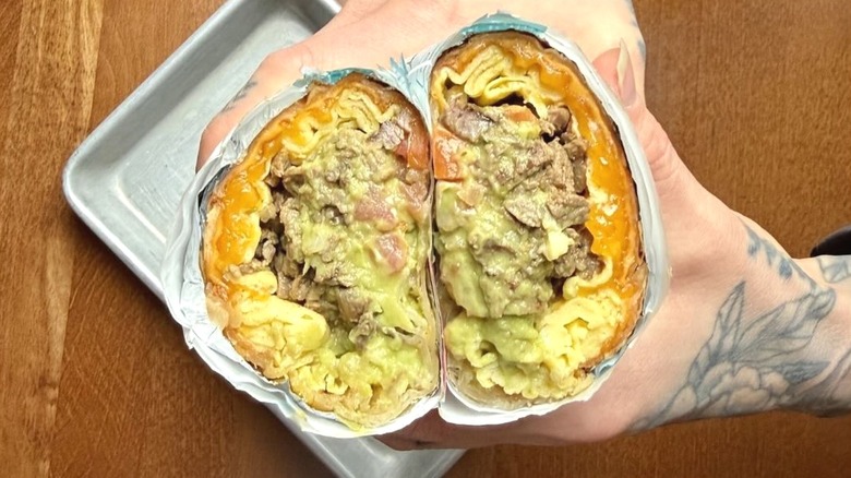 Tattooed hands holding large breakfast burrito