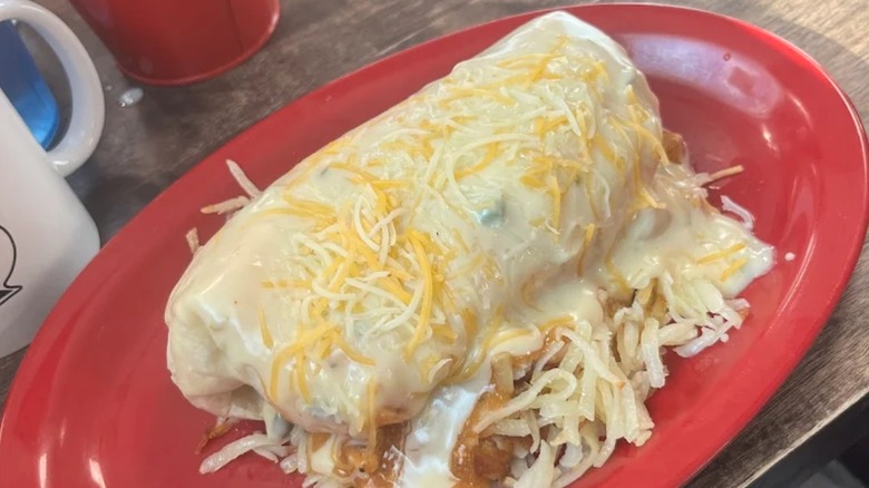 Massive breakfast burrito covered with cheese on hash browns