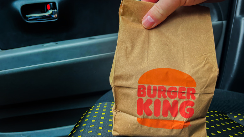 Hand holding Burger King takeout bag in car