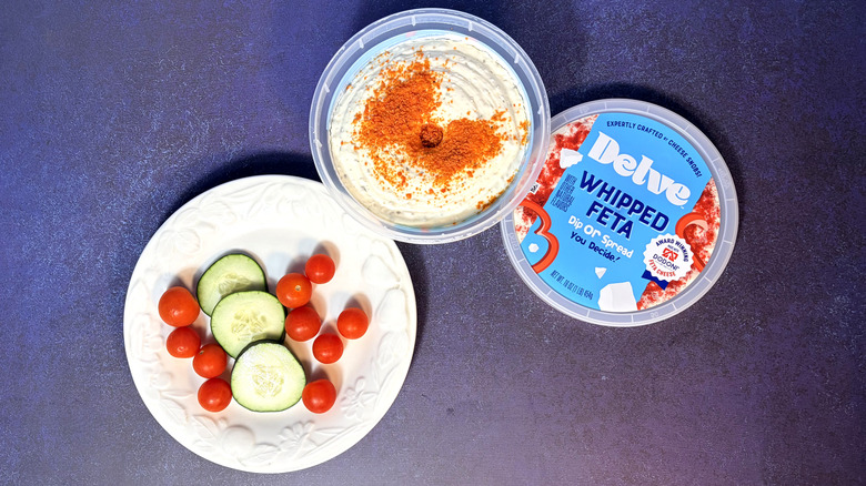 Opened package of delve whipped feta next to a plate with vegetables
