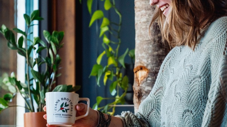 Woman smiling and holding a branded Evans Brothers coffee mug