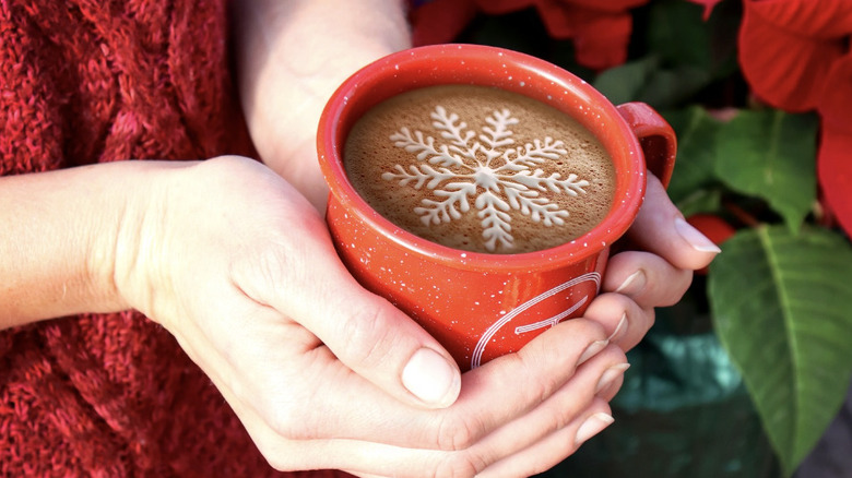 Hands holding red coffee mug with snowflake latte art