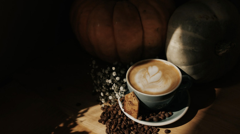 Shadowed image of latte in a mug surrounded by espresso beans