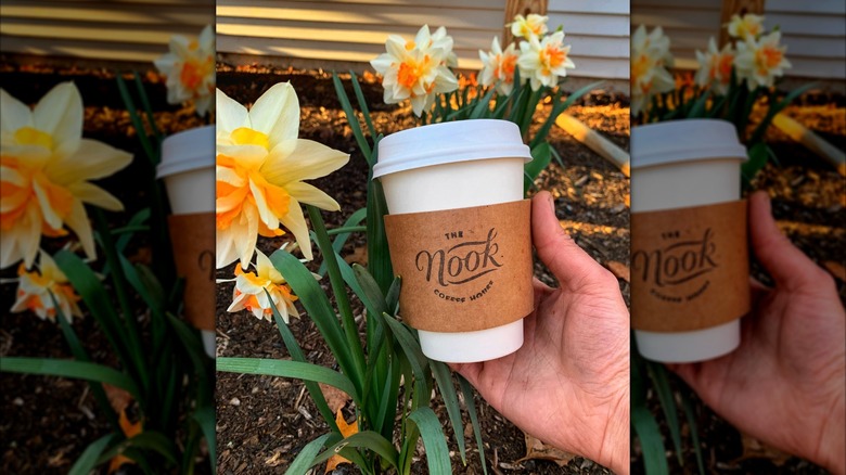 Hand holding The Nook coffee cup in front of yellow garden flowers