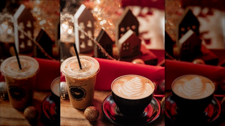 Hot latte in mug and iced latte set in front of red, cozy Christmas decor