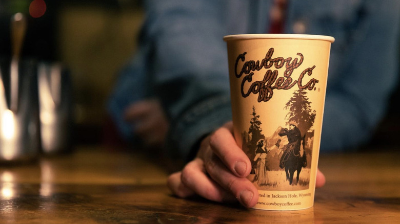 Hand holding Cowboy Coffee Co. branded cup on wooden table