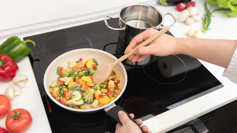 A person heating up vegetables in a pan on an induction stove