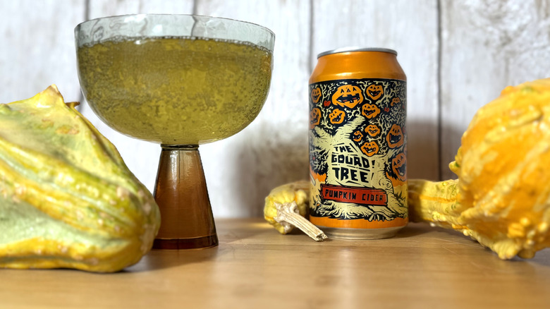 Can and glass of cider with decorative gourds