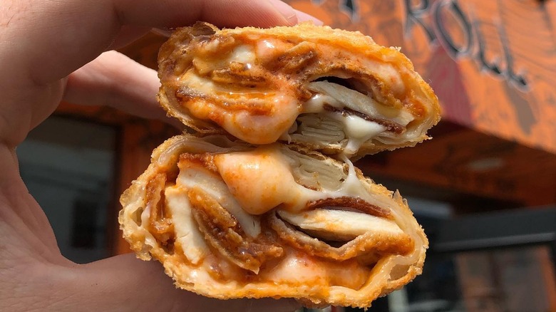 A hand holding two halves of a Verrazano Egg Roll from Wok n Roll