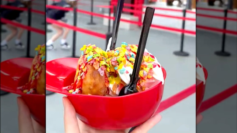 A hand holding a sundae in a baseball helmet, with toppings