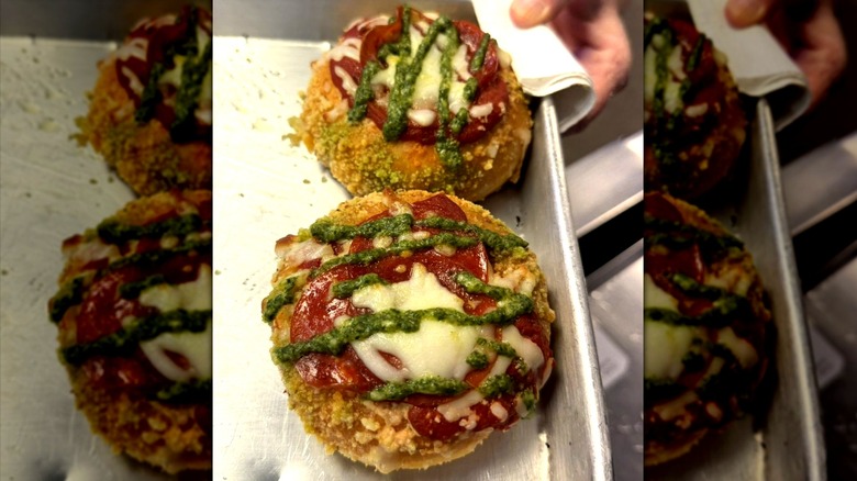 A hand holding a tray with two pizza donuts