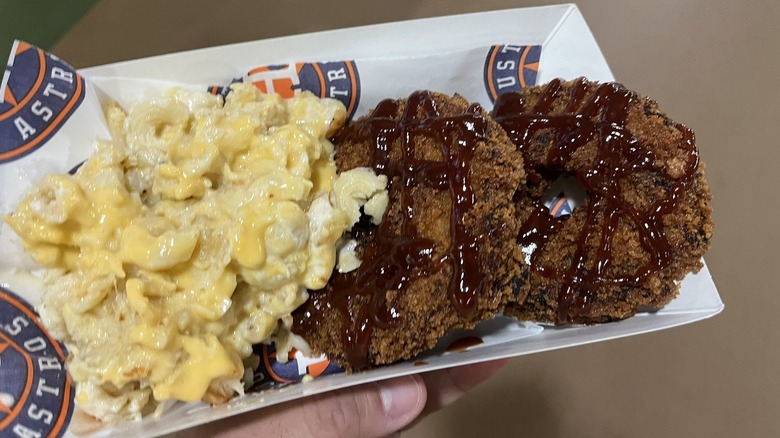 A hand holding a tray of brisket donuts and mac and cheese