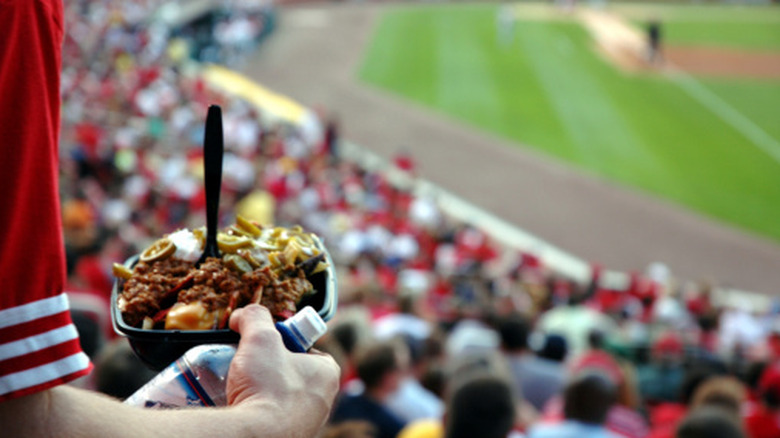 A fan holding a bowl of nachos and bottle of water in a baseball stadium stand