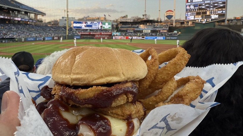 A fan in the stands, holding up a tray with a sandwich and onion rings