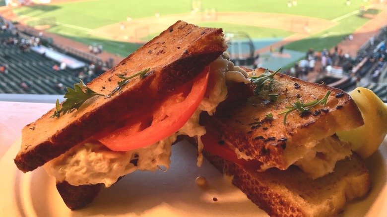 A crab sandwich on a plate, overlooking a baseball diamond