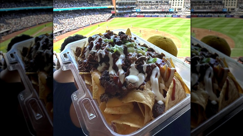 A tray of Tri-Tip nachos held in front of a baseball field