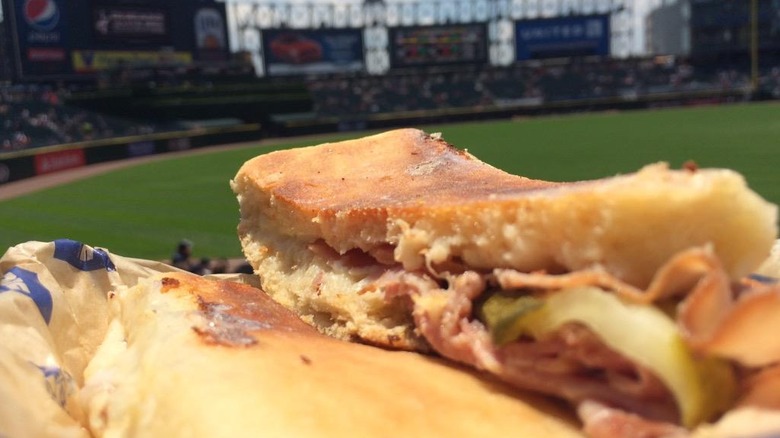 A close up of a sliced cuban sandwich with a ballpark in the background